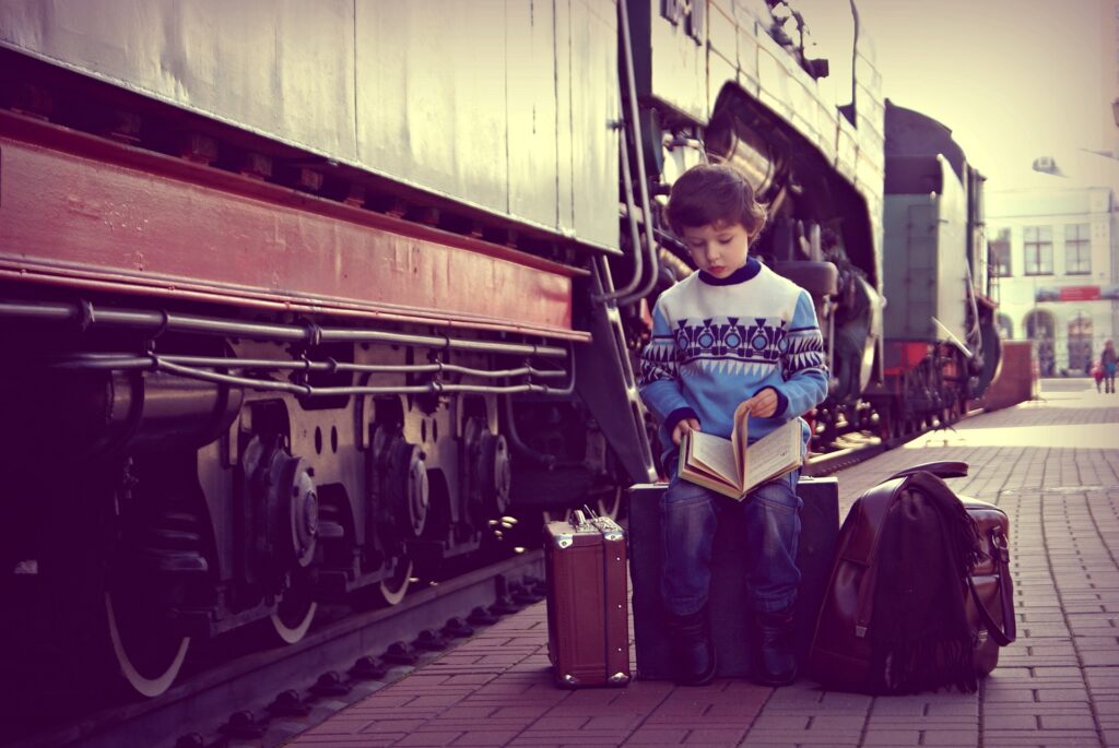 子供の電車の中の暇つぶし親子で楽しめるアイデア！5つのメリットもご紹介旅行中、電車のわきで本を読む男の子